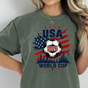 USA Soccer World Cup 2026 graphic shirt featuring soccer ball, American flag splash art, skyline design and patriotic football fan aesthetic