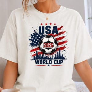 USA Soccer World Cup 2026 graphic shirt featuring soccer ball, American flag splash art, skyline design and patriotic football fan aesthetic
