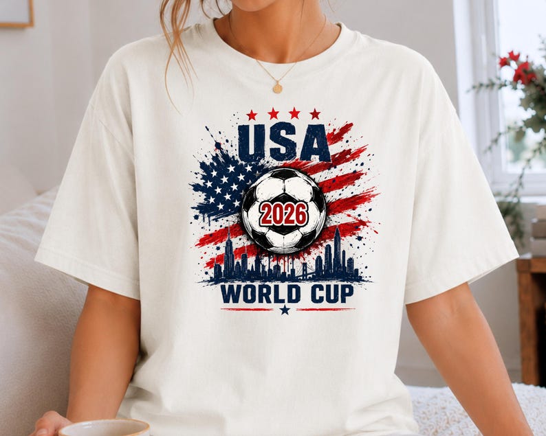 USA Soccer World Cup 2026 graphic shirt featuring soccer ball, American flag splash art, skyline design and patriotic football fan aesthetic