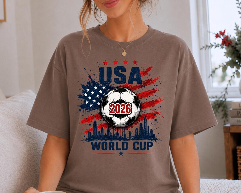 USA Soccer World Cup 2026 graphic shirt featuring soccer ball, American flag splash art, skyline design and patriotic football fan aesthetic
