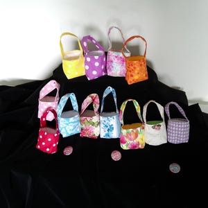 May include: A collection of small, fabric baskets with handles in various colors and patterns, including polka dots, floral prints, and solid colors. The baskets are arranged on a black surface.