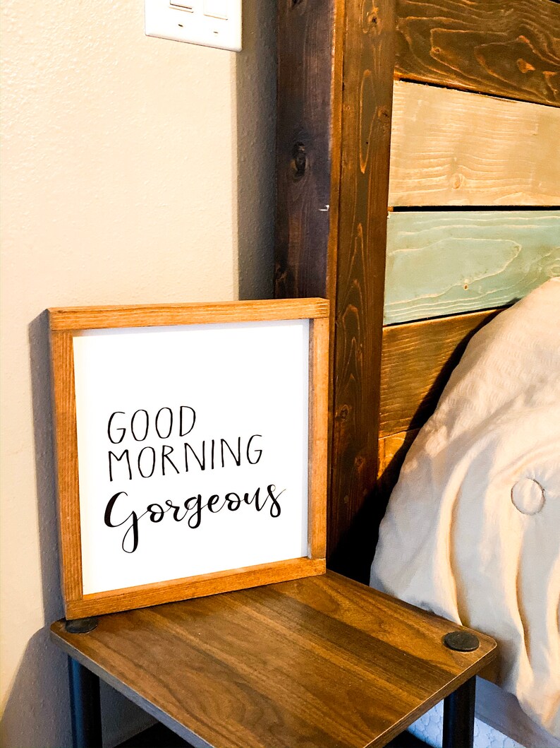 May include: A wooden framed sign with the text "Good Morning Gorgeous" in black script font on a white background.