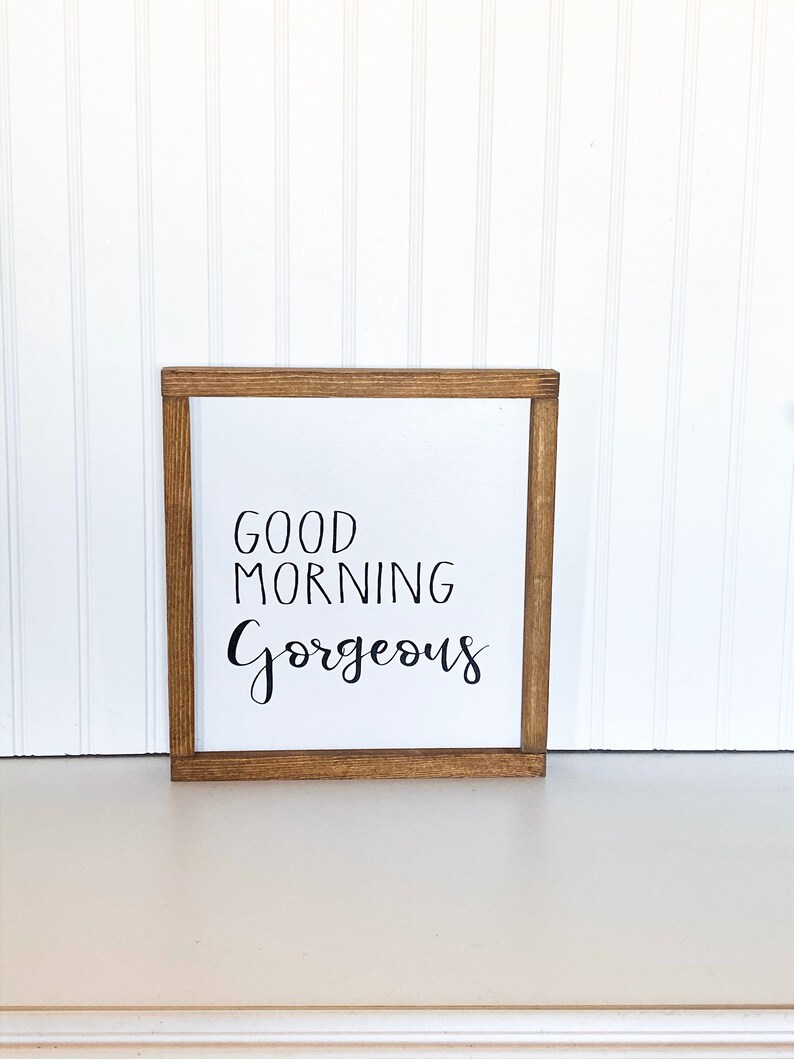 May include: A wooden framed sign with the text "Good Morning Gorgeous" in black calligraphy.