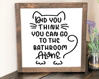 May include: A white wooden sign with a brown frame featuring a black cat illustration and the text "Did you think you can go to the bathroom alone?"