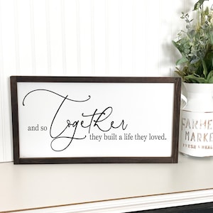 May include: A framed sign with a white background and black text that reads "and so together they built a life they loved."