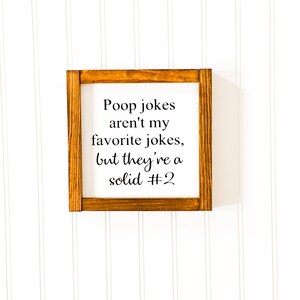 May include: A wooden sign with a brown frame and white background. The sign says "Poop jokes aren't my favorite jokes, but they're a solid #2".