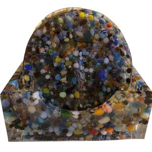 May include: Set of four colourful glass coasters with a variety of small, colourful glass pieces embedded in the resin. The coasters are in a holder made of the same material.