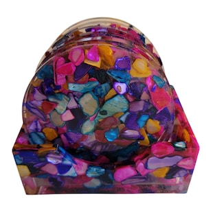 May include: Set of colorful coasters with a holder. The coasters are made of resin and have a variety of colors, including pink, purple, blue, and yellow. The holder is also made of resin and has a similar color scheme.