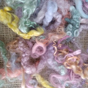 Könnte beinhalten: Ein Haufen bunter, flauschiger Wolle in den Farben Rosa, Blau, Grün und Gelb. Die Wolle ist in einem lockeren, verhedderten Haufen auf einem Jutesack-Hintergrund angeordnet.