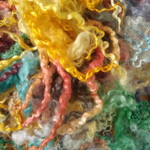 May include: A pile of colorful, curly fibers in shades of yellow, green, blue, pink, and white. The fibers are soft and fluffy, and they would be perfect for crafting or spinning.
