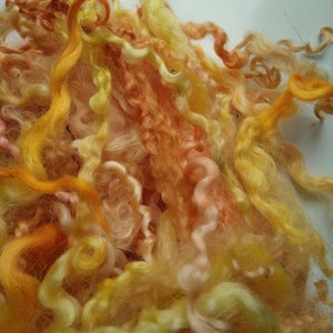 Puede incluir: Un montón de vellón de lana de color amarillo, naranja y melocotón. El vellón es suave y esponjoso y sería perfecto para hilar o fieltro.