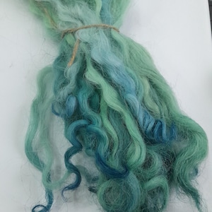 May include: A bundle of teal, blue, and green wool yarn. The yarn is soft and fluffy, and it is perfect for knitting or crocheting.
