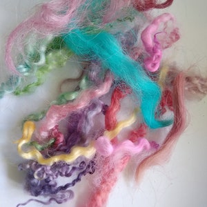 May include: A collection of colorful yarn strands in shades of pink, blue, green, yellow, and purple. The yarn is soft and fluffy, and it would be perfect for knitting or crocheting.