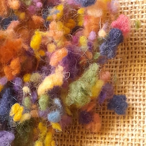 Può includere: Primo piano di un mucchio di fibre di lana colorate in tonalità di arancione, giallo, verde, blu e viola. Le fibre sono disposte in un mucchio sciolto e soffice e sembrano essere tinti a mano.