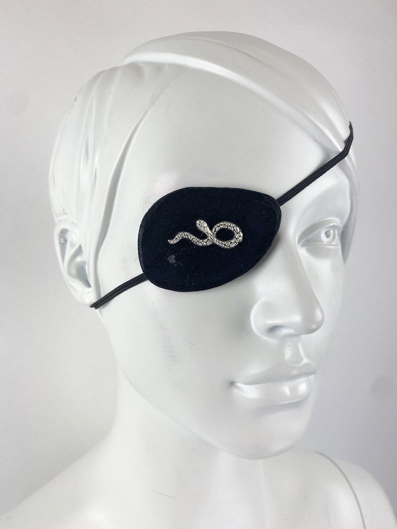 May include: A black eye patch with an embroidered silver snake design. The eye patch is held in place with an elastic strap.