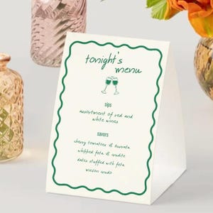 May include: A white table menu card with a green, wavy border. The text "tonight's menu" is at the top, with a wine glass graphic. The menu lists "sips" and "savors" with food and drink options.