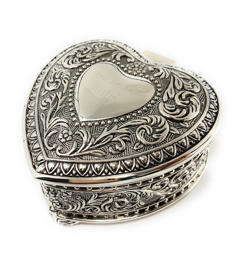 May include: A silver heart-shaped trinket box with an ornate design and an engraved inscription that reads "Audie Mae and David".