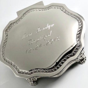 May include: Silver keepsake box with a scalloped edge and three feet. The lid is engraved with the text "Ava Jordyn Baptized 12-24-2018".