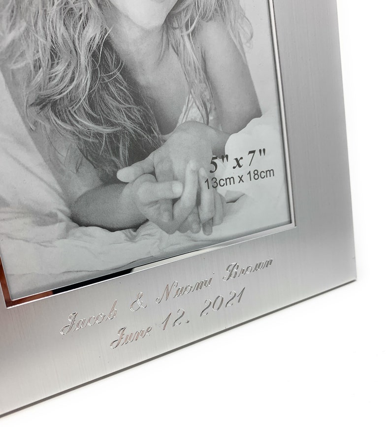 May include: Silver photo frame with a black and white photo of a couple holding hands. The frame is engraved with the text "Jacob & Naomi Brown June 12, 2021" and the dimensions "5" x 7" 13cm x 18cm".