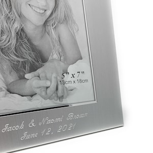 May include: Silver photo frame with a 5x7 inch (13cm x 18cm) opening. The frame has a brushed finish and is engraved with the text "Jacob & Naomi Brown June 12, 2021".