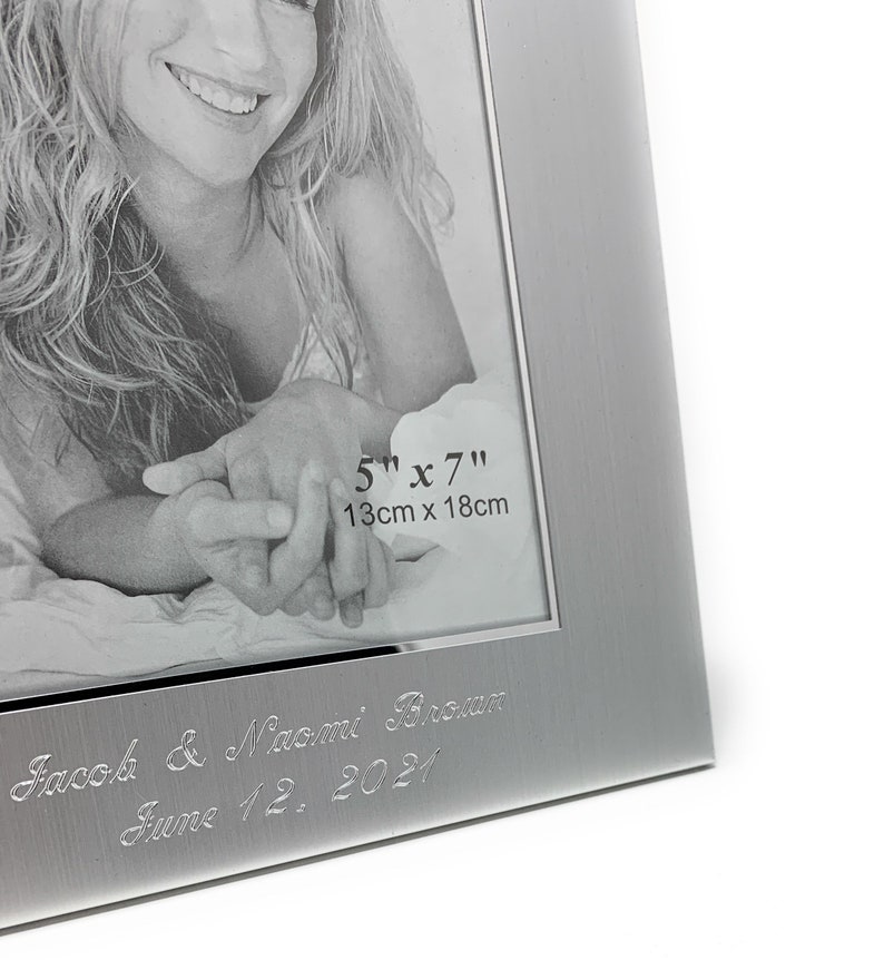 May include: Silver photo frame with a 5x7 inch (13cm x 18cm) opening. The frame has a brushed finish and is engraved with the text "Jacob & Naomi Brown June 12, 2021".