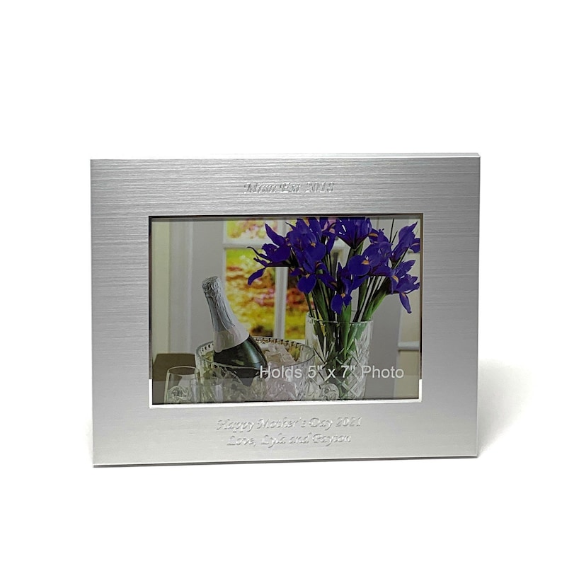 May include: Silver photo frame with a brushed finish. The frame holds a 5 x 7 inch photo and has the text "Happy Mother's Day 2021 Love, Luke and Peyton" engraved on the bottom.