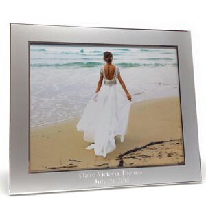 May include: Silver picture frame with a white mat and a photo of a bride walking on a beach. The frame is engraved with the text "Claire Victoria Thomas July 31, 2013".