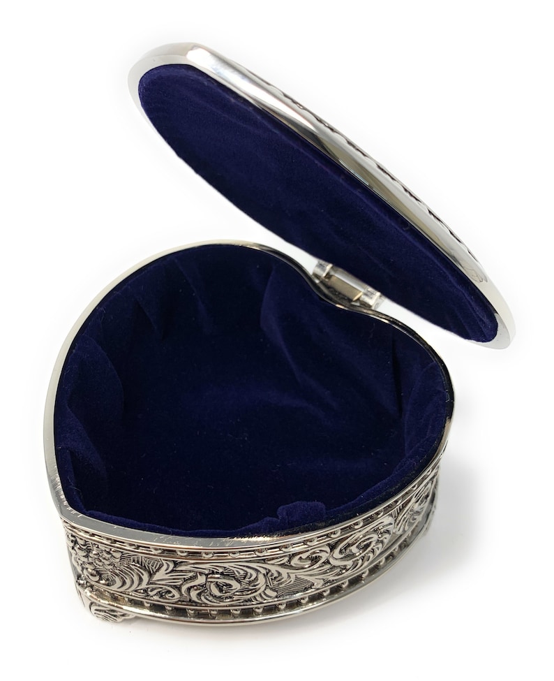 May include: A silver heart-shaped trinket box with an ornate design and a blue velvet interior. The lid is open, revealing the empty interior.