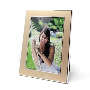 May include: A gold picture frame with a silver border and a white mat. The frame has a photo of a woman in a hammock. The frame is engraved with the text "Show Strength".