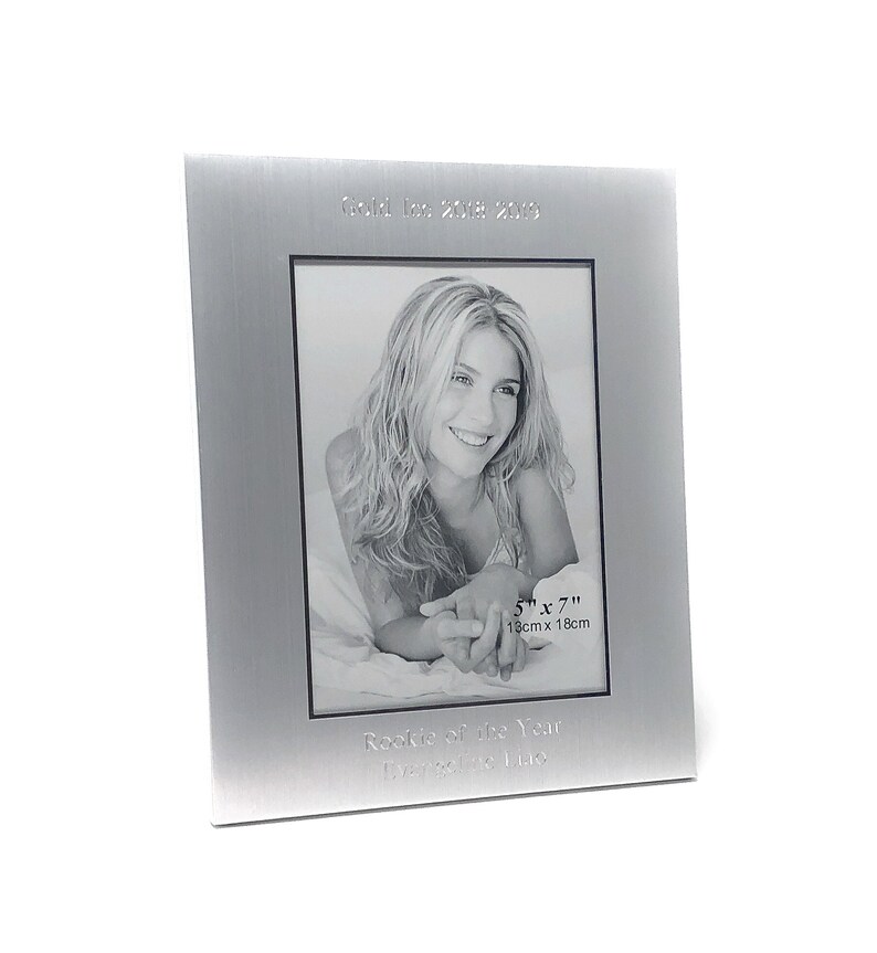 May include: Silver photo frame with a black and white photo of a woman. The frame has the text "Gold Team 2018-2019" and "Rookie of the Year,  [Name]" engraved on it. The photo is 5" x 7" (13cm x 18cm).