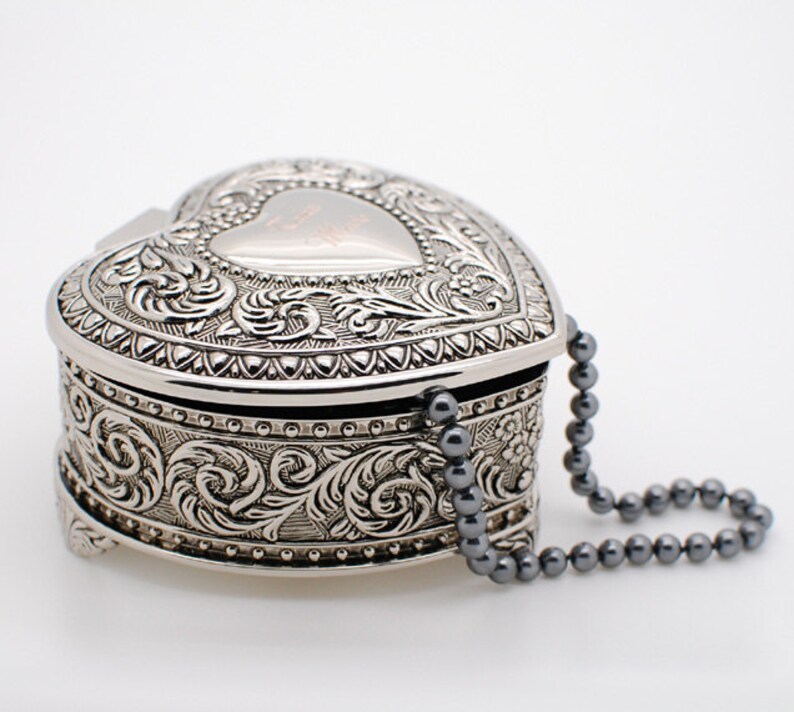 May include: A silver heart-shaped trinket box with an ornate design and a beaded chain.