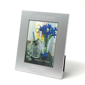May include: Silver picture frame with a brushed finish. The frame holds a 13x18 cm photo of a bouquet of blue irises in a vase, a bottle of champagne in a bucket of ice, and two champagne flutes. The frame is engraved with the text "A New Core Memory", "Holds 5" x 7" Photo", "Mikaels & Kare", and "July 11, 2021".