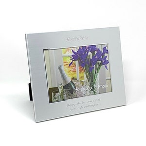 May include: Silver picture frame with a white mount and a 5x7 inch photo of purple flowers in a vase. The frame has the text "Established 2022" and "Holds 5x7 Photo" engraved on it. The frame also has the text "Happy Mother's Day, Mum, you're my world. Love, [Name]" engraved on it.