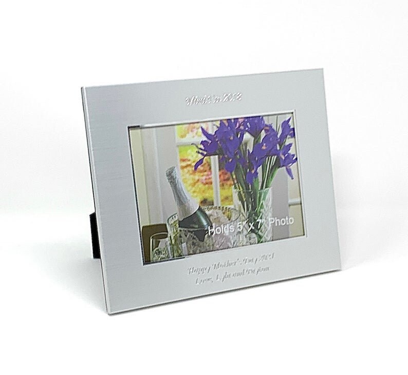 May include: Silver picture frame with a white mount and a 5x7 inch photo of purple flowers in a vase. The frame has the text "Established 2022" and "Holds 5x7 Photo" engraved on it. The frame also has the text "Happy Mother's Day, Mum, you're my world. Love, [Name]" engraved on it.