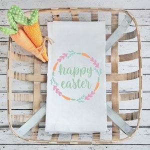 May include: A white kitchen towel with a green and pink wreath design and the text "happy easter" in the center.