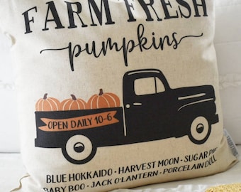 May include: A beige square pillow with the words "FARM FRESH pumpkins" in black script. A black truck graphic carries three orange pumpkins. The text "OPEN DAILY 10-6" is on a banner. Additional text includes pumpkin varieties.