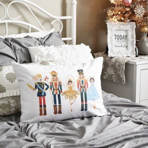 May include: White decorative pillow featuring a colorful illustration of nutcracker characters. The pillow is placed on a bed with gray bedding. A white framed sign that says "TODAY I WILL BE HAPPIER french fry" is on a nightstand.