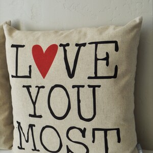 May include: A beige pillow with the words "I LOVE YOU MOST" printed in black with a red heart in place of the "O" in "LOVE".