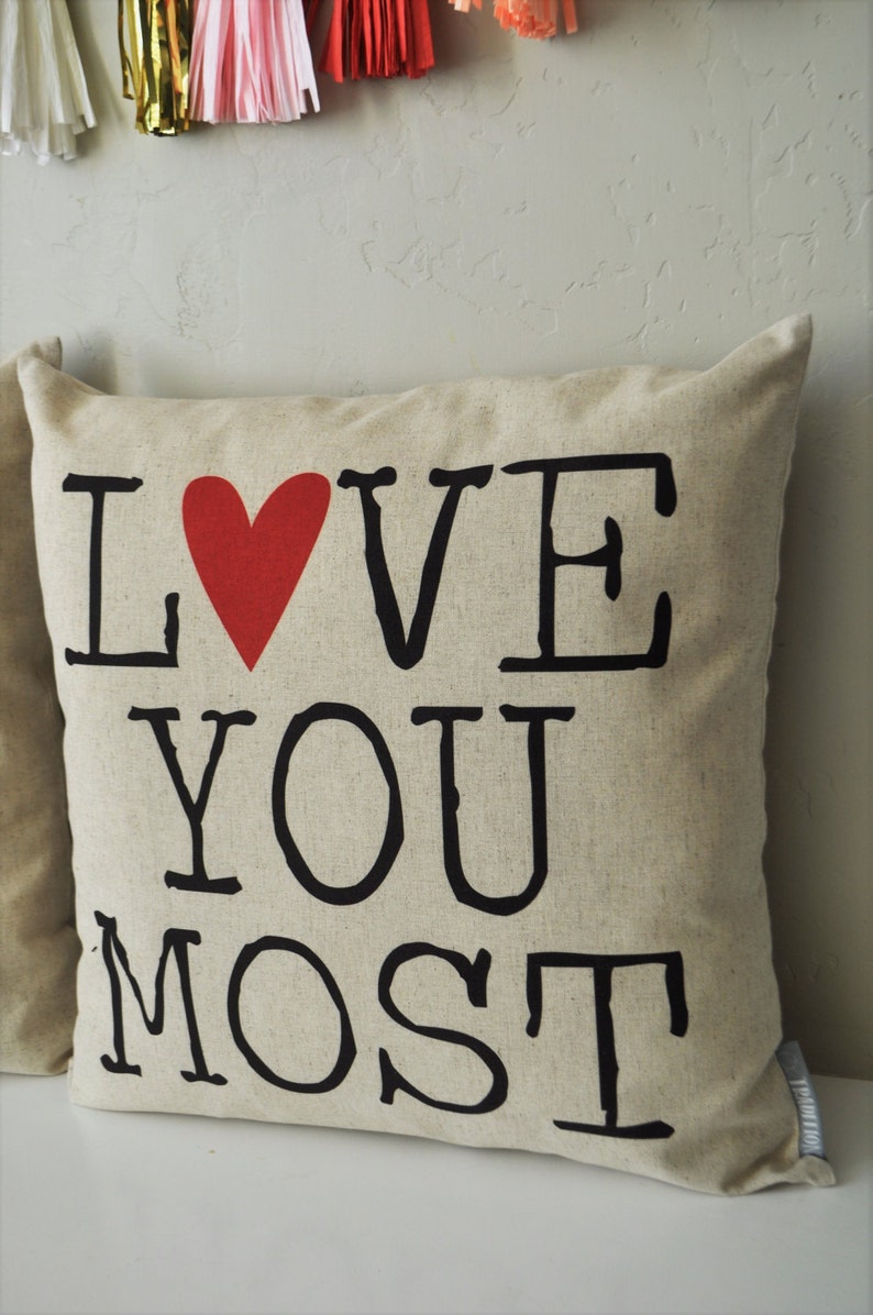 May include: A beige pillow with the words "I LOVE YOU MOST" printed in black with a red heart in place of the "O" in "LOVE".