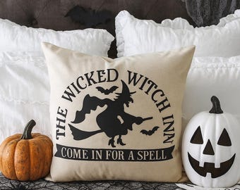 May include: A Halloween-themed scene featuring a decorative pillow with a witch design and the text "The Wicked Witch Inn Come in for a Spell." An orange pumpkin and a white jack-o'-lantern are also present.