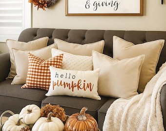 May include: A cozy living room scene with a gray sofa adorned with beige and patterned pillows. A wooden sign reads "Let our lives be full of both thanks & giving." A metal tray holds pumpkins and pinecones.