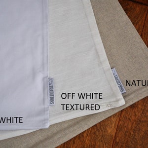 May include: Three fabric swatches in varying shades of white and beige are displayed. The swatches are labeled "Bright White", "Off White Textured", and "Natural". Each swatch has a small tag that reads "Traditions".