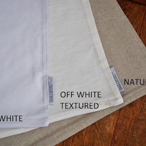 May include: Three fabric swatches in varying shades of white and beige are displayed. The swatches are labeled "Bright White", "Off White Textured", and "Natural". Each swatch has a small tag that reads "Traditions".