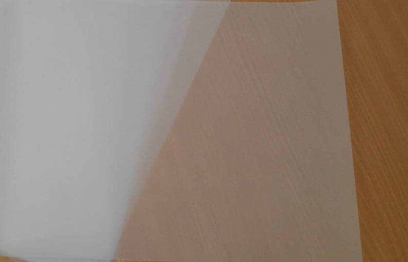 May include: A sheet of white translucent paper, folded in half, on a wooden surface.