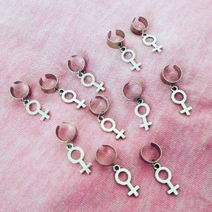 Puede incluir: Diez pinzas para el pelo plateadas con un colgante en forma de s&iacute;mbolo femenino. Las pinzas est&aacute;n dise&ntilde;adas para sujetar el pelo.
