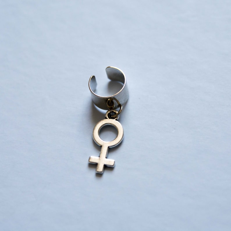 Puede incluir: Pendiente de aro de plata con un dije colgante en forma de s&iacute;mbolo femenino.