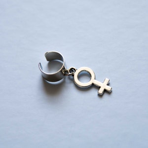 Puede incluir: Pendiente de aro de plata con un colgante de plata en forma de s&iacute;mbolo femenino.