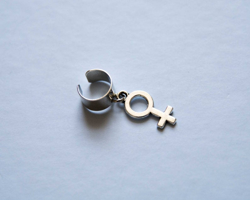 Puede incluir: Pendiente de aro de plata con un colgante de plata en forma de s&iacute;mbolo femenino.