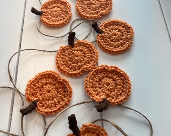 Puede incluir: Una guirnalda de calabazas tejidas a ganchillo en naranja, con tallos marrón oscuro. Las calabazas están ensartadas con hilo, creando una decoración otoñal rústica. Cada calabaza mide unos 7 cm de diámetro.