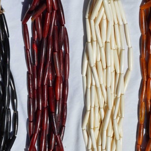 May include: Four strands of beads, each a different color: black, red, white, and orange. The beads are all cylindrical and have a slightly rounded shape.